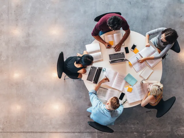 Overhead view of a team collaborating around a table with laptops and documents